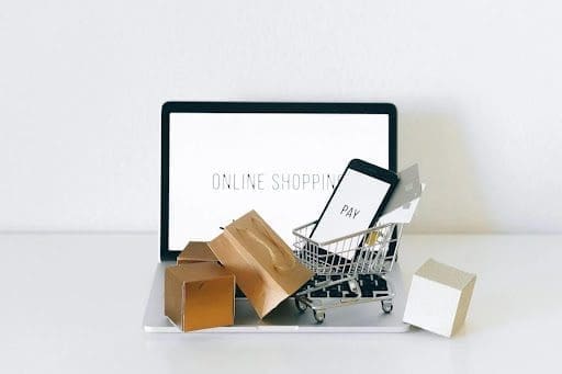 A miniature shopping cart on a laptop that reads “online shopping”.